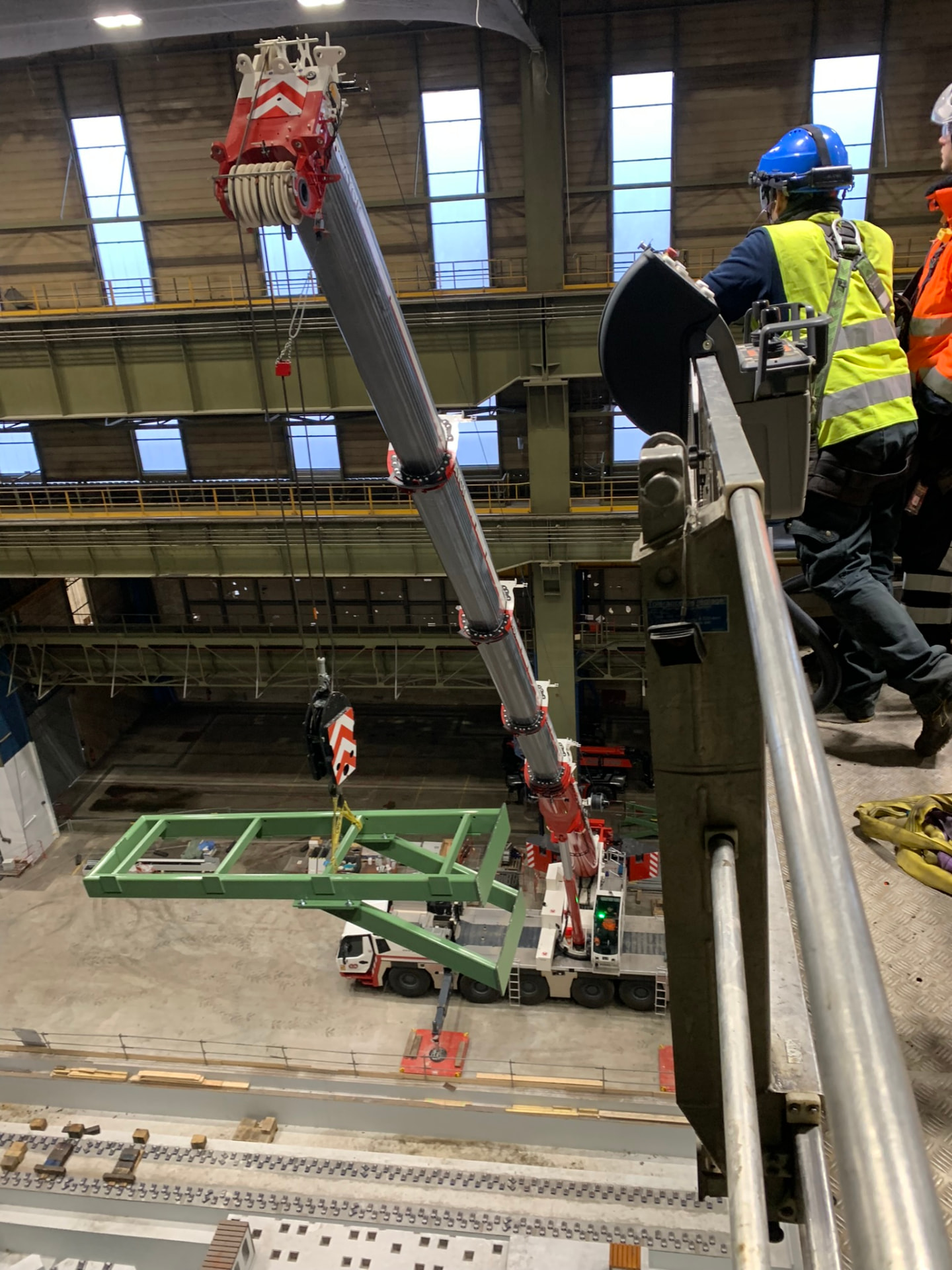 Intervenants équipés depuis une nacelle, supervisant une opération de levage dans un hall industriel